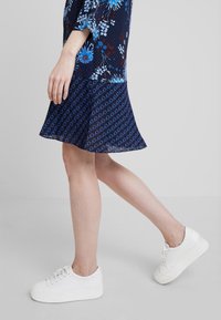 Námořnické květinové šaty s krátkým rukávem, zdobené modrým kruhovým vzorem. Spárovány s bílými platformovými teniskami.