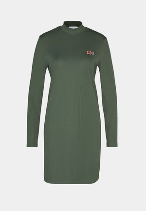 Robe verte à manches longues avec un col haut, fabriquée en tissu côtelé. Présente un petit logo lacoste brodé sur la poitrine.