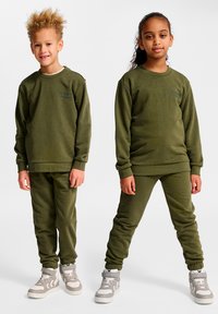 Grünes Sweatshirt und Jogginghosen-Set für Kinder, mit gerippten Bündchen, Rundhalsausschnitt und Seitentaschen, kombiniert mit grauen Turnschuhen.