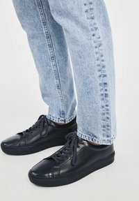 Czarne skórzane trampki o gładkiej strukturze, okrągłym nosku i płaskiej podeszwie, zestawione z jasnoniebieskimi dżinsami o prostym kroju.