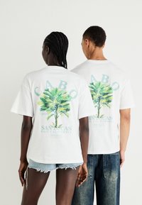 Valge puuvillane T-särk, mille seljal on palmipuu graafika. Omab tekstide "CABO", "SAN LUCAS" ja "BAJA CALIFORNIA" pastellvärvides.