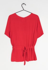 Blusa rossa leggera con maniche corte e larghe; vita arricciata con un accento legato; texture liscia e design a girocollo semplice.