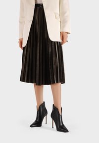 Stivaletti neri in pelle con punta appuntita e cerniere laterali, caratterizzati da un sottile tacco a stiletto. Indossati con una gonna nera plissettata e un blazer bianco.