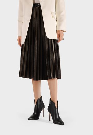 Stivaletti neri in pelle con punta appuntita e cerniere laterali, caratterizzati da un sottile tacco a stiletto. Indossati con una gonna nera plissettata e un blazer bianco.
