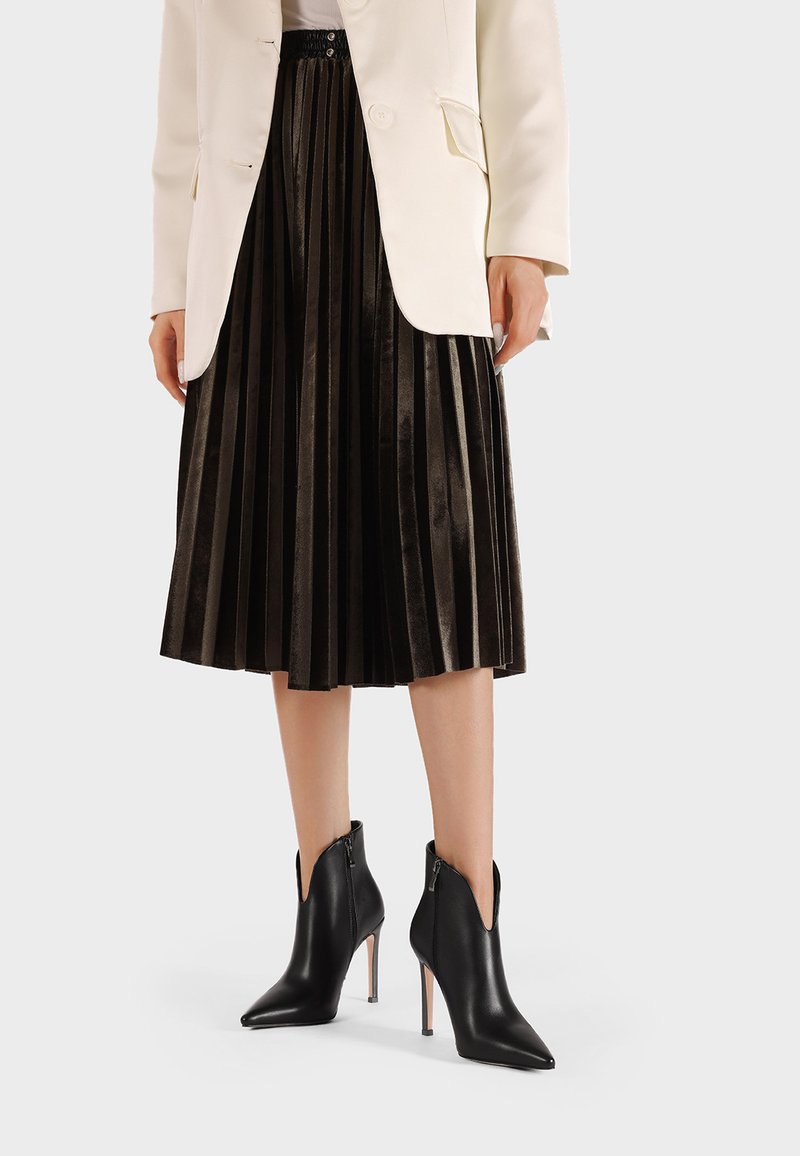 Stivaletti neri in pelle con punta appuntita e cerniere laterali, caratterizzati da un sottile tacco a stiletto. Indossati con una gonna nera plissettata e un blazer bianco.