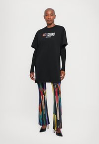 Juodas medvilninis per didelis T-shirt su "Moschino Jeans" logotipu; ryškiai marginti platėjančio kirpimo kelnės su sagtimis. Juodi uždari aukšti kulniukai užbaigia įvaizdį.
