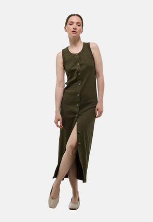 Robe midi sans manches vert olive avec un devant à boutons, une fente sur le côté et une texture côtelée. Portée avec des chaussures de couleur claire.
