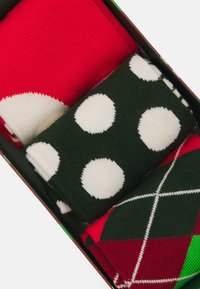 Set di tre paia di calzini: rosso con cerchio bianco, verde con pois bianchi e un motivo argyle rosso e verde. Materiale in maglia morbido, design compatto.