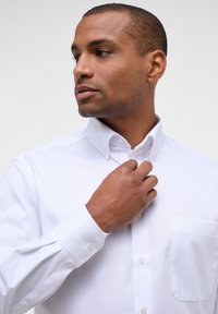 Camicia bianca con colletto strutturato, taschino singolo sul petto e bottoni perlacei, realizzata in morbido cotone e con maniche lunghe.