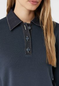 Granatowa, ribbed shirt z dżinsowym kołnierzykiem, z trzema ciemnymi guzikami i kontrastowym przeszyciem. Zbliżenie na kołnierzyk.