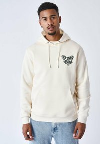 Sudadera crema con bolsillo frontal, capucha ajustable y gráfico de mariposa en verde oscuro en el lado izquierdo del pecho. Tejido suave, corte relajado.