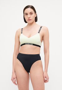 Svetlozeleno modrček z V-izrezom, z črnimi naramnicami in črnim pasom s logotipom "Calvin Klein". Črne bikinije s visokim pasom.