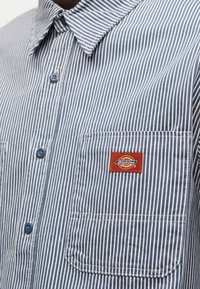 Μπλε και άσπρο πουκάμισο με κάθετες ρίγες, γιακά, κουμπιά και μπροστινή τσέπη με κόκκινο σήμα Dickies.