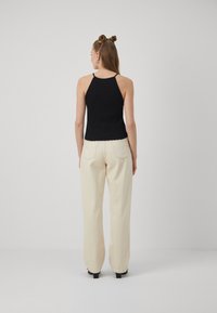 Black ribbed tank top with spaghetti straps paired with high-waisted, wide-leg cream trousers. Smooth texture and neutral colors.