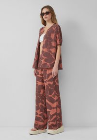 Twee-delig outfit met een knoopshirts met korte mouwen en wijde broek in aardse tinten van roest met abstracte patronen. Getextureerde stof.