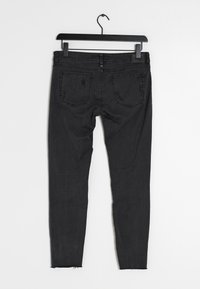 Jeans negros con corte ajustado, hechos de mezclilla. Presentan un dobladillo desflecado, dos bolsillos traseros y un ligero desgaste cerca de la parte superior y los bolsillos.