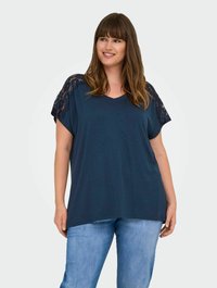 Navy blue V-neck top with lace accents on shoulders, relaxed fit, and soft texture. Paired with light blue jeans.