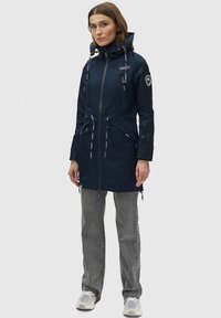 Navy blue waterproof jacket with adjustable hood, drawstring waist, and zippered pockets. Features branded accents and a sleek design.