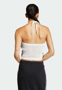 Bílý síťovaný krátký top s halterovým výstřihem a otevřenými zády, ve spojení s černou žebrovanou sukní s bočními pruhy a elastickým pasem.