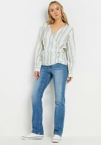 Blusa de manga larga, estilo cruzado, con rayas verdes claras y blancas. Combinada con jeans azules y zapatillas blancas. Textura de tela suave.