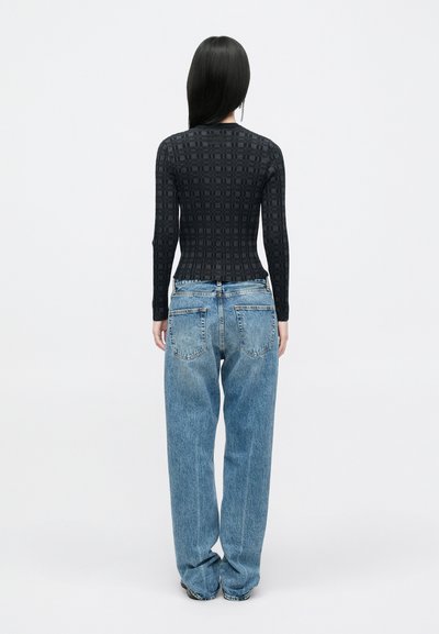 Top lung cu mânecă lungă, texturat, de culoare neagră, cu un model în grilaj, asortat cu blugi din denim de culoare albastru deschis, lejeri, cu un design clasic cu cinci buzunare.