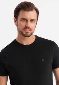 Czarna, krótko rękawowa koszulka z gładkiej bawełny, z okrągłym dekoltem i małym logo na piersi.