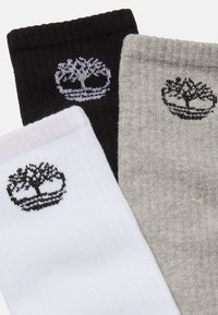 Tre par sokker: sort, grå og hvid. Hver har et logo af et træ broderet i kontrastfarver. Blødt, tekstureret stof med ribbet design.