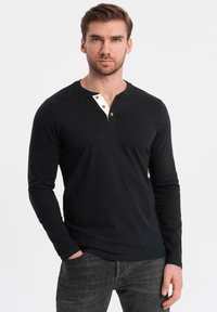 Zwarte longsleeve shirt met een contrasterende witte hemdkraag en drie houten knopen bij de hals. Eenvoudig, aansluitend ontwerp.