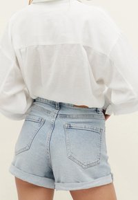 Camisa blanca, ligera y de botones con yugo trasero, combinada con shorts de mezclilla azul claro con puños enrollados y bolsillos traseros.