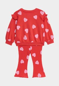 Rød bomulds to-dels sæt med en pullover med lyserøde hjerte mønstre og rynkede ærmer, parret med ribbenede flared leggings med matchende print.
