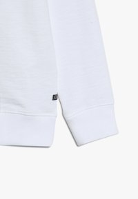 Felpa bianca con polsini a costine, in morbido tessuto di cotone, e una piccola etichetta nera sul bordo. Design semplice e classico con texture.