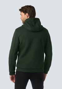 Donkergroen hoodie van textiel met een gestructureerde stof, ribgebreide boorden en onderkant. Heeft een grote capuchon. Zichtbare stiksels langs de schouders en zijkanten.