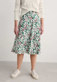 Floral midi skirt with green background, featuring white, pink, and red flowers. Styled with a textured cream sweater and beige sneakers.