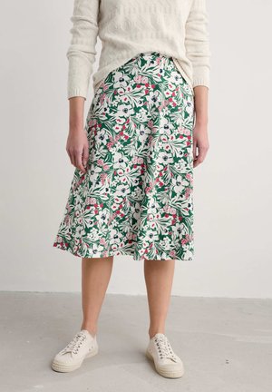 Bloemige midi-rok met groene achtergrond, versierd met witte, roze en rode bloemen. Gestyled met een textuurachtig crèmekleurig sweater en beige sneakers.