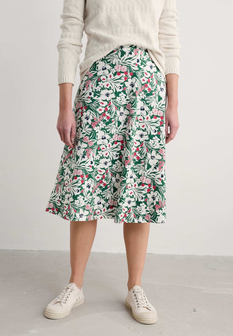 Floral midi skirt with green background, featuring white, pink, and red flowers. Styled with a textured cream sweater and beige sneakers.