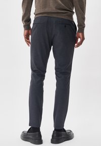 Dunkelgraue, schmal zulaufende Hose aus strukturiertem Stoff, mit zwei hinteren Taschen und glattem Bund. Kombiniert mit schwarzen Schuhen.