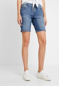 Džínové šortky v světle modré barvě, s pěti kapsami, zapínání na knoflíky, ohrnutým lemem a běžným střihem. Doplněné o bílé tenisky.