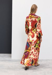 Abito lungo a fiori con una combinazione di colori rossi, gialli e verdi. Realizzato in tessuto leggero con vestibilità ampia e maniche lunghe.