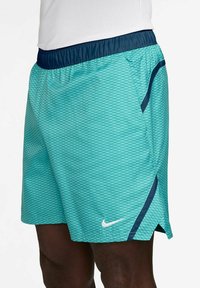 Turquoise athletic shorts with diamond pattern, elastic waistband in navy, side pocket with navy accent, and white logo detail on front.