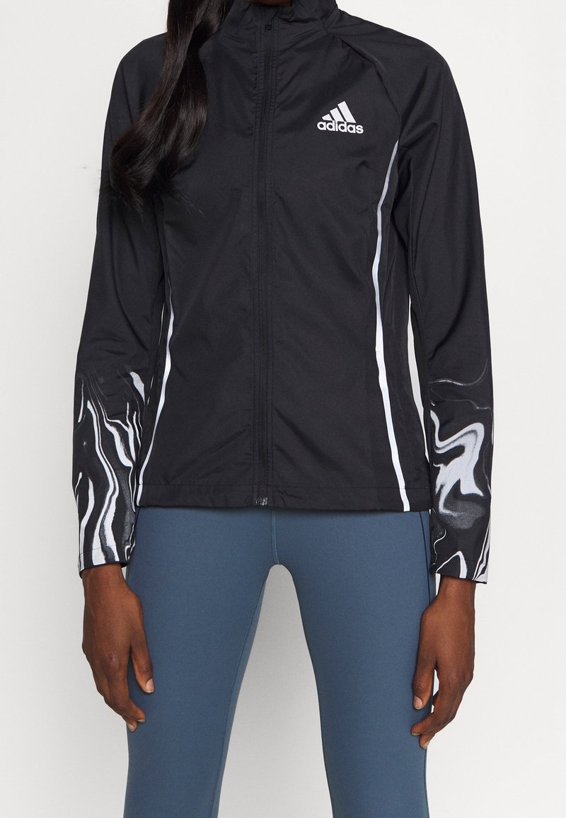 Musta Adidas-takki, jossa on kokovetoketju, valkoiset yksityiskohdat ja marmorin kuvioidut hihat. Kevyt, istuva malli, joka sopii aktiiviseen käyttöön.