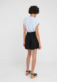 Blouse à manches courtes bleu clair, short noir à taille élastique et sandales noires avec plateforme en bois. Tissu lisse, coupe décontractée et shorts jusqu'aux genoux.