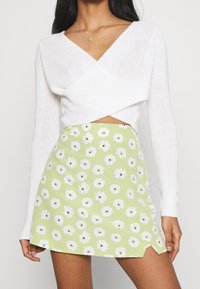 White knitted cropped sweater with long sleeves paired with a green A-line skirt featuring a white floral pattern and side slit.