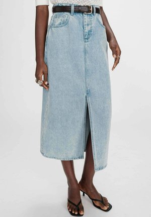 Femme portant une jupe midi en denim bleu clair avec une fente devant, une ceinture noire, un haut en maille blanc et des sandales à talons noires.