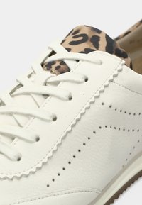 Λευκό δερμάτινο παπούτσι με σχεδίαση σε σχήμα κυμάτων, με λεπτομέρεια από ύφασμα με λεοπάρ σχέδιο στη φτέρνα και λευκά επίπεδα κορδόνια.