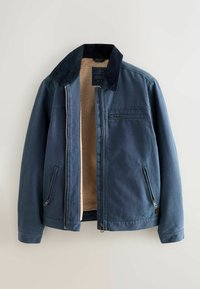 Chaqueta azul marino con cuello negro, cremallera delantera parcialmente abierta que revela el forro de sherpa beige, y tres bolsillos externos con cremallera.