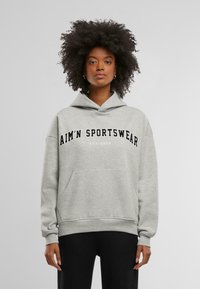 Szürke kapucnis pulóver kenguruzsebbel, oversize fazonban, fekete betűkkel "AIM'N SPORTSWEAR EST. 2013" felirattal a mellkason. Puha szövet textúra.