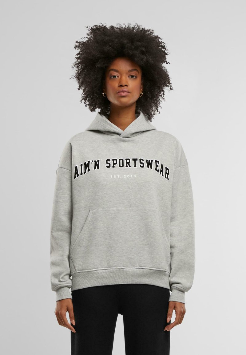 Szürke kapucnis pulóver kenguruzsebbel, oversize fazonban, fekete betűkkel "AIM'N SPORTSWEAR EST. 2013" felirattal a mellkason. Puha szövet textúra.