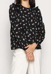 Blusa nera con stampa floreale, caratterizzata da maniche arricciate e scollatura rotonda. Realizzata in tessuto leggero, con una vestibilità ampia e rilassata.