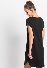 Abito nero a maniche corte con una vestibilità rilassata, realizzato in materiale morbido. Presenta maniche arrotolate e fessure laterali per facilitare i movimenti.