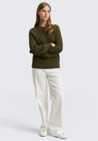 Oliwkowy sweter prążkowany z długimi rękawami, w połączeniu z białymi spodniami o szerokich nogawkach i białymi trampkami; gładka tekstura, luźny krój.